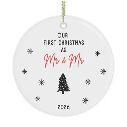 A round white ceramic Christmas ornament gift for gay couple with a hanging loop, featuring the printed text 'OUR FIRST CHRISTMAS AS Mr & Mr' in black and red, a black Christmas tree, and '2026' at the bottom, surrounded by small black snowflakes on a white background.