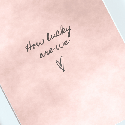 Close-up of handwritten How Lucky Are We typography on a blush watercolour print