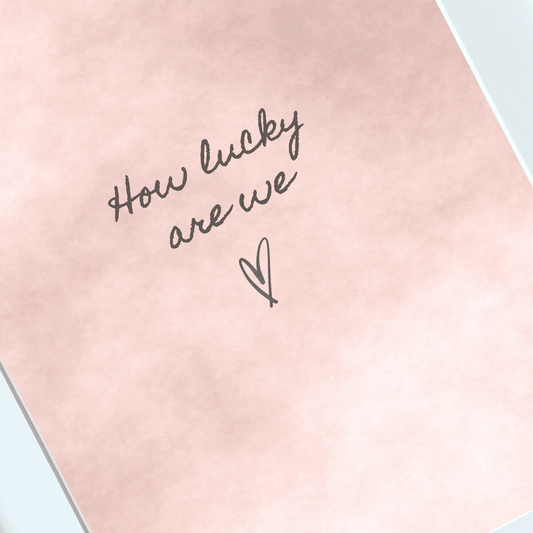 Close-up of handwritten How Lucky Are We typography on a blush watercolour print