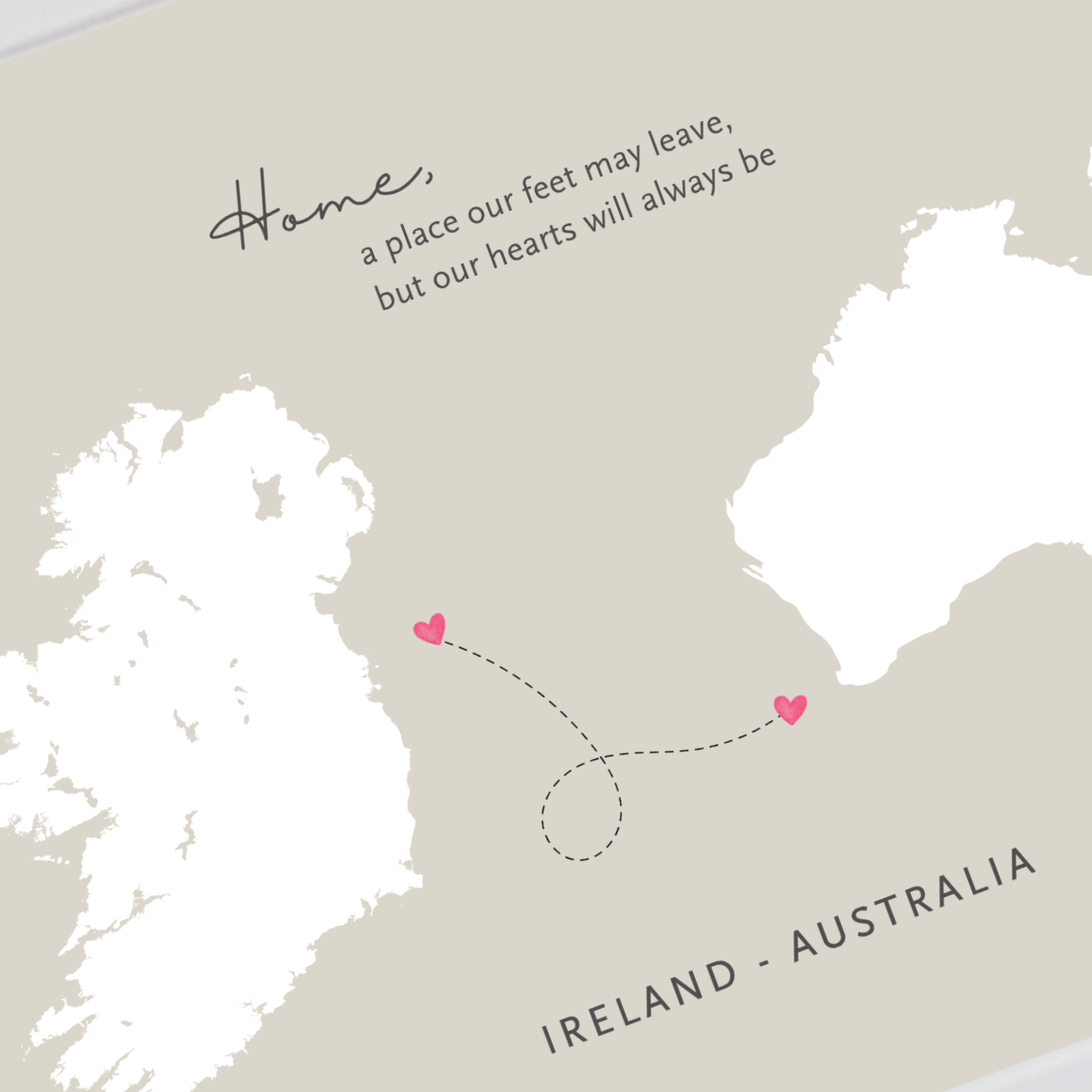 A minimalist map print with Ireland and Australia in white, a dotted dashed line connecting two small pink hearts, and the text 'Home, a place our feet may leave, but our hearts will always be' above, plus 'IRELAND - AUSTRALIA' at the bottom on a warm beige background.