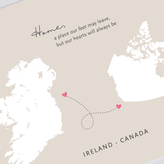 A minimalist travel map print featuring Ireland and Canada in white silhouette shapes on a warm beige background, with a dotted dashed line connecting two small pink hearts and a quote above reading, 'Home, a place our feet may leave, but our hearts will always be.'.