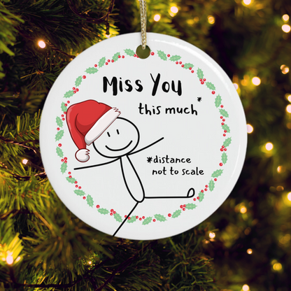Round Christmas ornament with a stick figure wearing a Santa hat, holly wreath and the message “Miss You This Much – distance not to scale”.