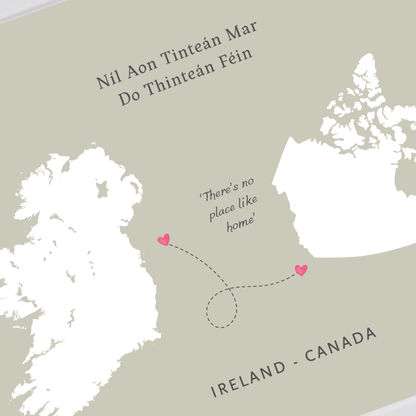 A minimalist map-style print showing Ireland and Canada, with the text 'Nil Aon Tinteán Mar Do Thinteán Féin' at the top, 'There's no place like home' in the center, and 'IRELAND - CANADA' at the bottom. Two small pink hearts mark locations on the map.