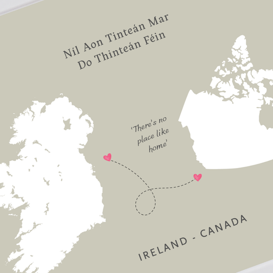 A minimalist map-style print showing Ireland and Canada, with the text 'Nil Aon Tinteán Mar Do Thinteán Féin' at the top, 'There's no place like home' in the center, and 'IRELAND - CANADA' at the bottom. Two small pink hearts mark locations on the map.