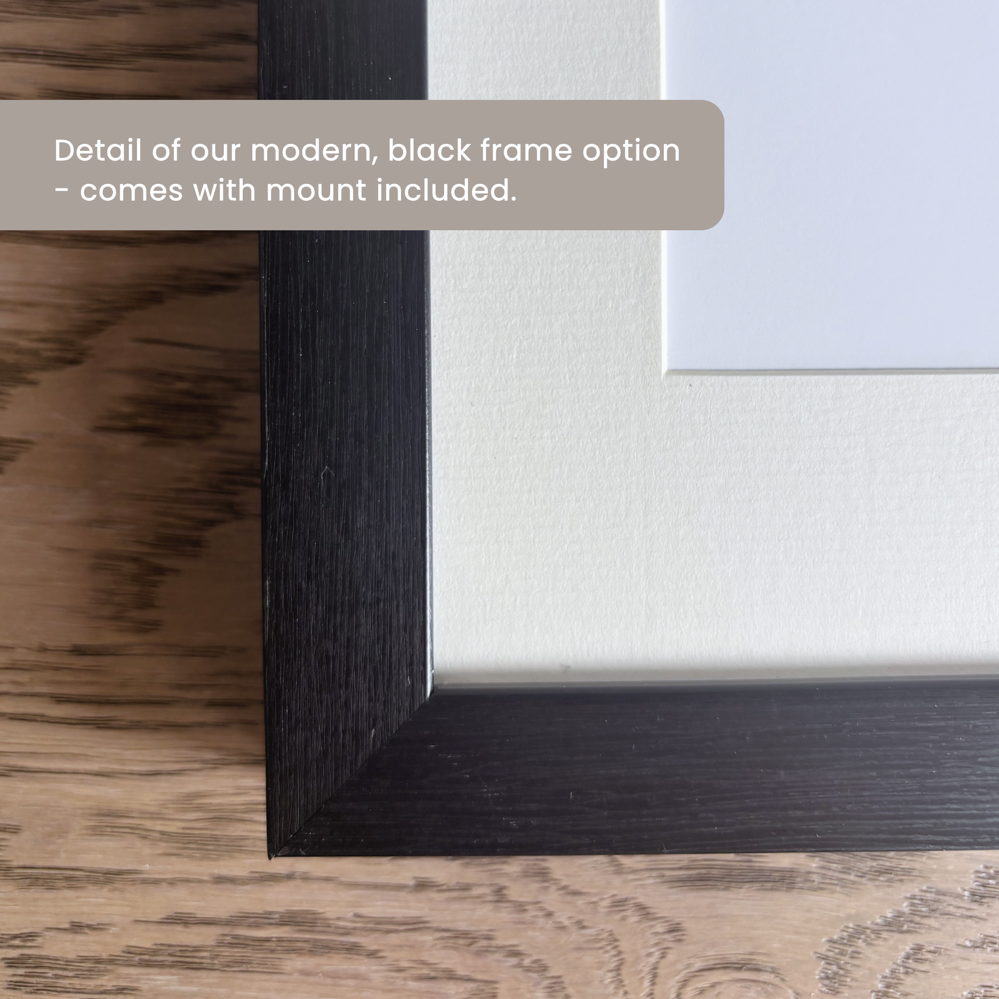 Close-up corner of a willow and moon black frame option with a white matt board. text overlay reading 'Detail of our modern, black frame option - comes with mount included.'.